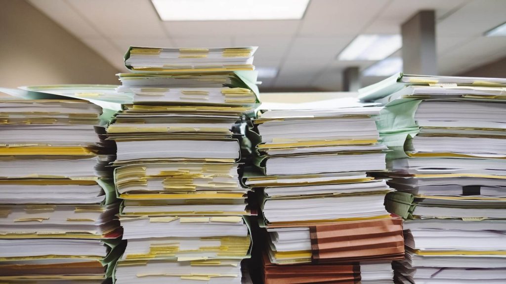 A cluttered scene with stacks of paperwork, suggesting a busy or organizational task.